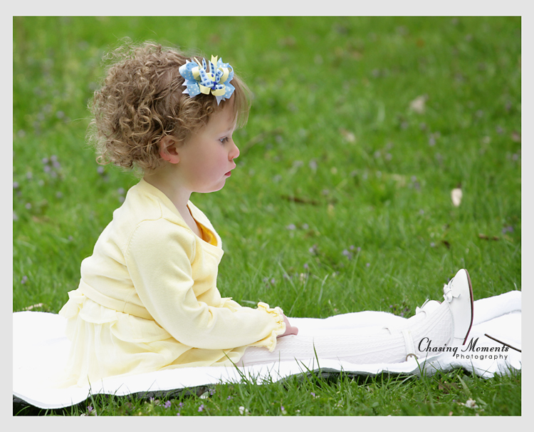 Little girl in a yellow Easter, spring outfit sitting on grass in a park in McLean, VA