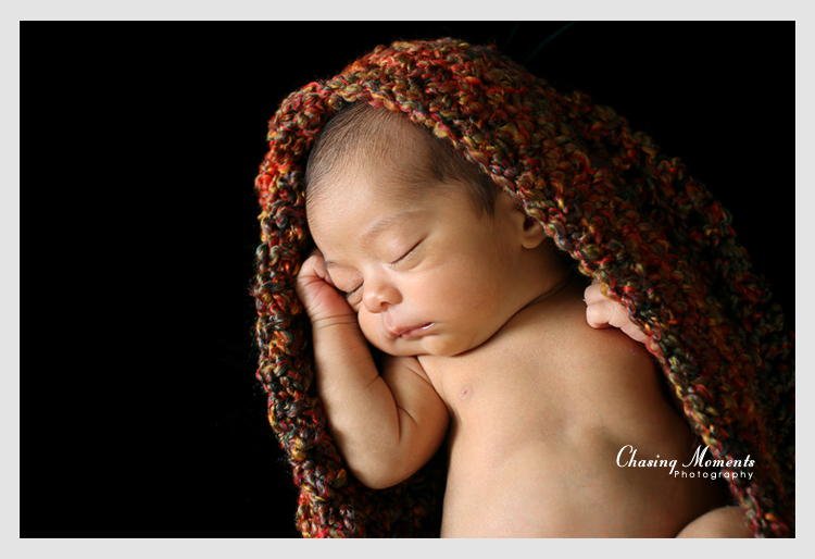 newborn asleep in a knit wrap on black background