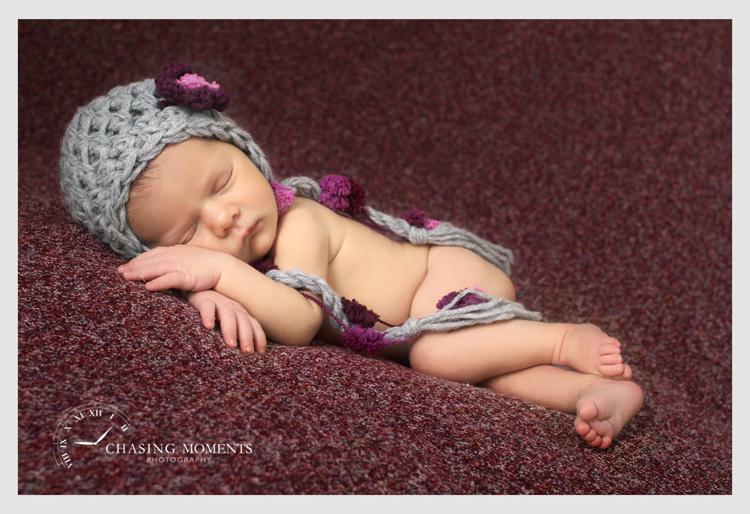 newborn baby girl asleep in a vintage knit hat on cranberry fabric backdrop