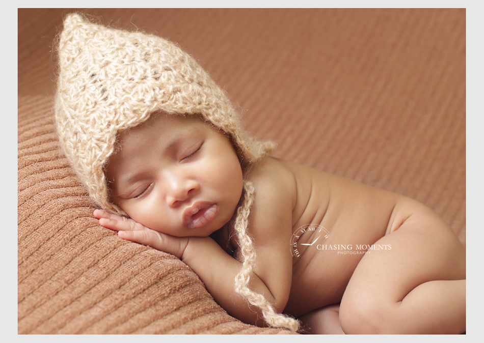 newborn baby girl asleep posed on a brown blanket wearing a bonnet